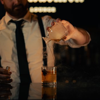 Houndsmen Lounge male bartender pouring smoke onto a whiskey sour.