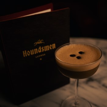 Espresso martini in front of Houndsmen Lounge leather menu on marble table.