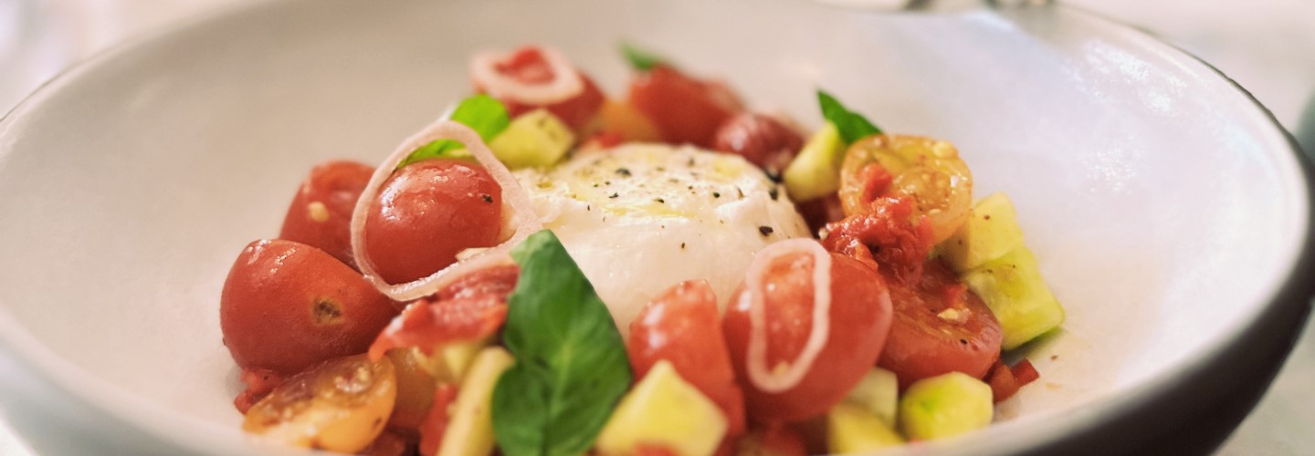 Burrata with cherry tomatoes, cucumbers, and basil in a white serving dish.