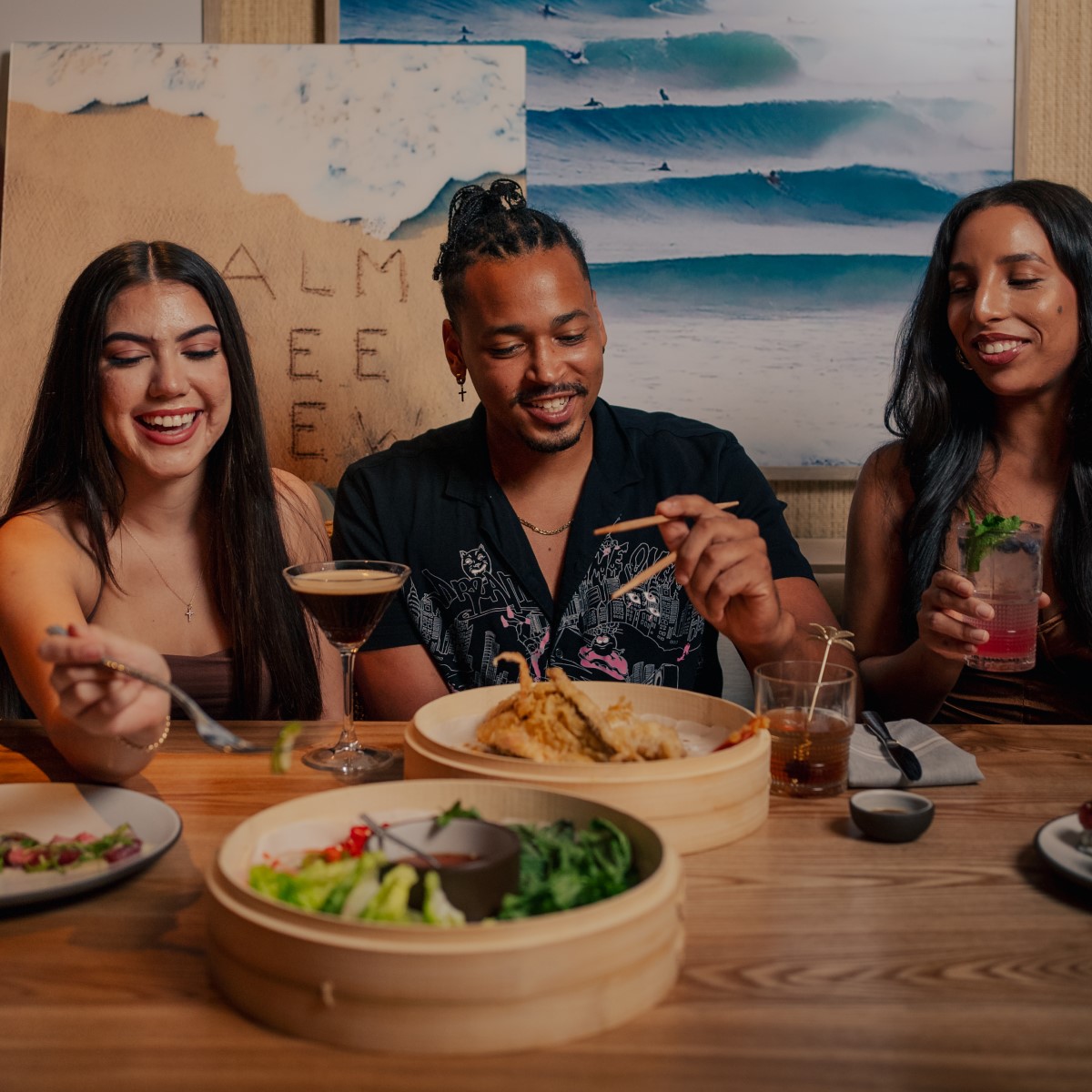 Two women and a man enjoying Asian dishes and cocktails.