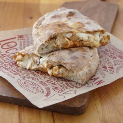 Sal's Pizza buffalo chicken calzone cut in half and stacked on a paper wrapper and wooden serving board.