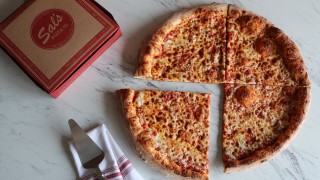 Cheese pizza cut in four slices next to Sal's Pizza box, napkin, and serving spatula.