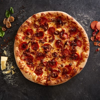 Sal's Pizza meat lover's whole pie on a black counter with pepperoni, sausage, basil, and small block of parmesan cheese on either side.