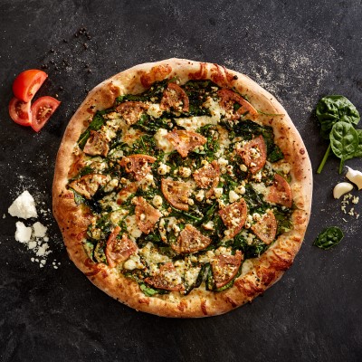 Sal's Pizza spinach and feta whole pie on a black counter with tomato, spinach, garlic, and feta cheese on either side.